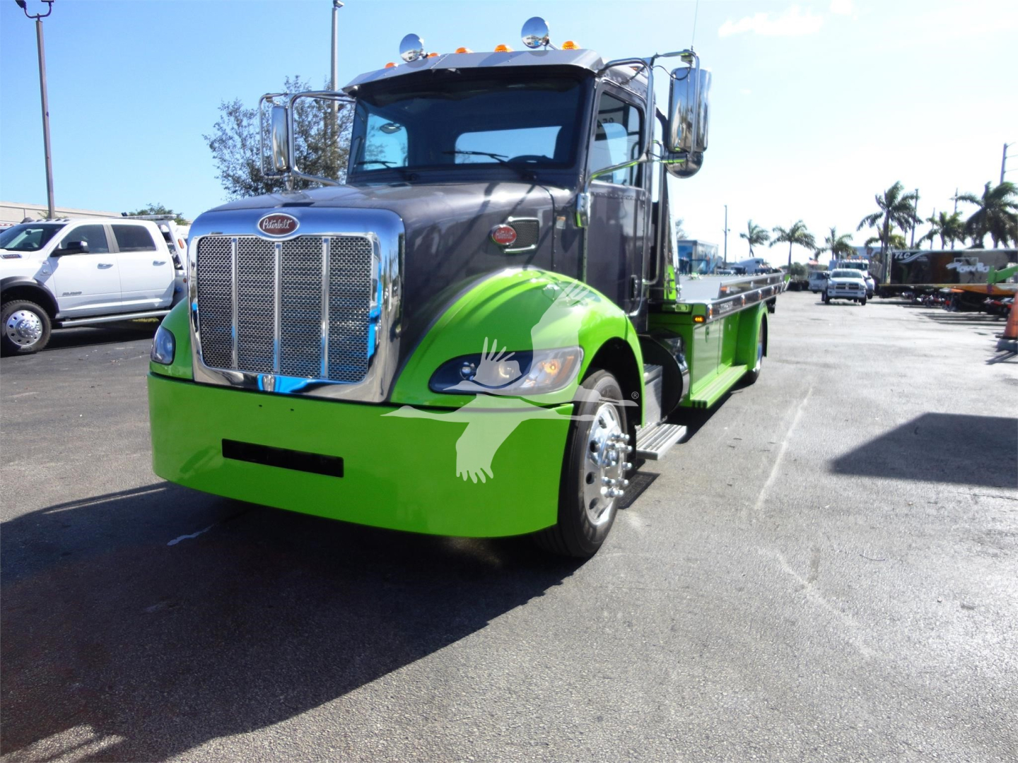 Peterbilt 337 rollback truck front view showing bright green bumper and chrome grille with black hood, rear flatbed, chrome mirrors, and chrome exhaust stacks.