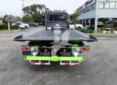Back view of a 2022 Peterbilt 337 rollback truck with a flatbed and bright green bumper accents.