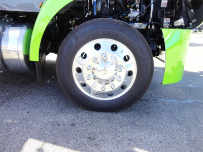 Peterbilt 337 front wheel and green fender showing chrome wheel with multiple lug nuts and tire, engine bay area visible.