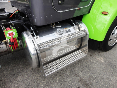 Truck fuel tank with polished chrome cylindrical tank and metal diamond-plate steps mounted under a bright green Peterbilt cab.