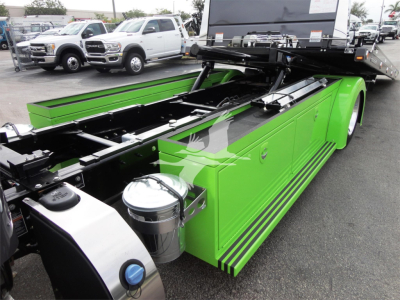 Green Peterbilt rollback truck bed with hydraulic frame and storage compartments, side rail panels, and chrome fuel tank cap visible.