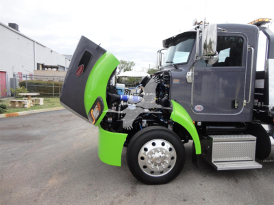 Peterbilt 337 rollback truck with hood open, showing engine bay and green fender; front wheel and chrome steps visible.