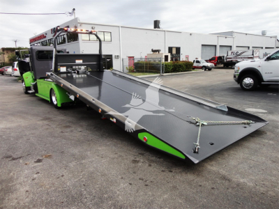 Peterbilt 337 rollback tow truck with a lowered flatbed in the foreground, green accents, stock number J56626, dealership lot in background