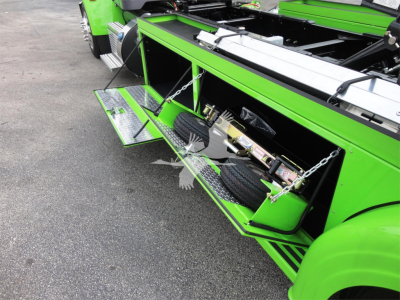 Peterbilt 337 rollback truck with bright green body and open side tool compartments showing steps and auxiliary equipment.