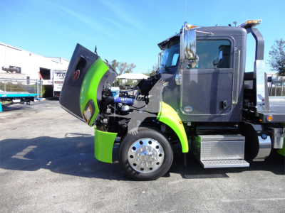 Peterbilt 337 rollback truck with hood open, showing green accent panels and chrome wheel, cab door visible, engine bay exposed.