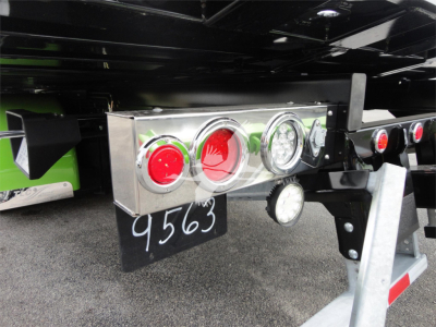 Rear view of a 2022 Peterbilt 337 rollback truck showing a chrome taillight panel with red and white circular lights and a small round gauge, black mud flap with number 9563, and metal bumper supports.