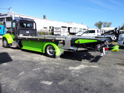 Peterbilt 337 rollback tow truck in lime green and black, side view with flatbed, branding and equipment visible in a lot.