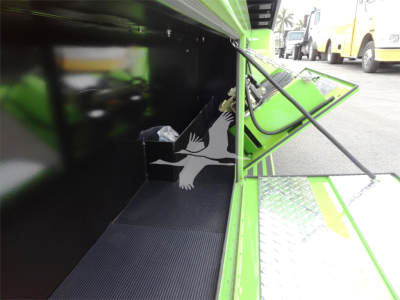 Truck bed area inside a green Peterbilt rollback unit showing a black interior panel and a small storage compartment with a plastic bag.
