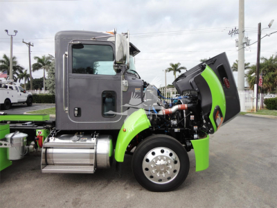 Peterbilt 337 rollback truck with hood open, showing engine components and modern green accent, front wheel and side step visible.