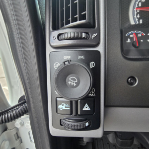 Dashboard left switch panel of a 2027 Mack PI64T showing headlight control dial, fog lights, and trailer brake/parking switch.