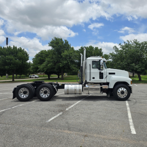 Truck side profile: 2027 Mack PI64T conventional daycab tractor, white cab, chrome exhaust stacks, fuel tanks, and dual rear axles.