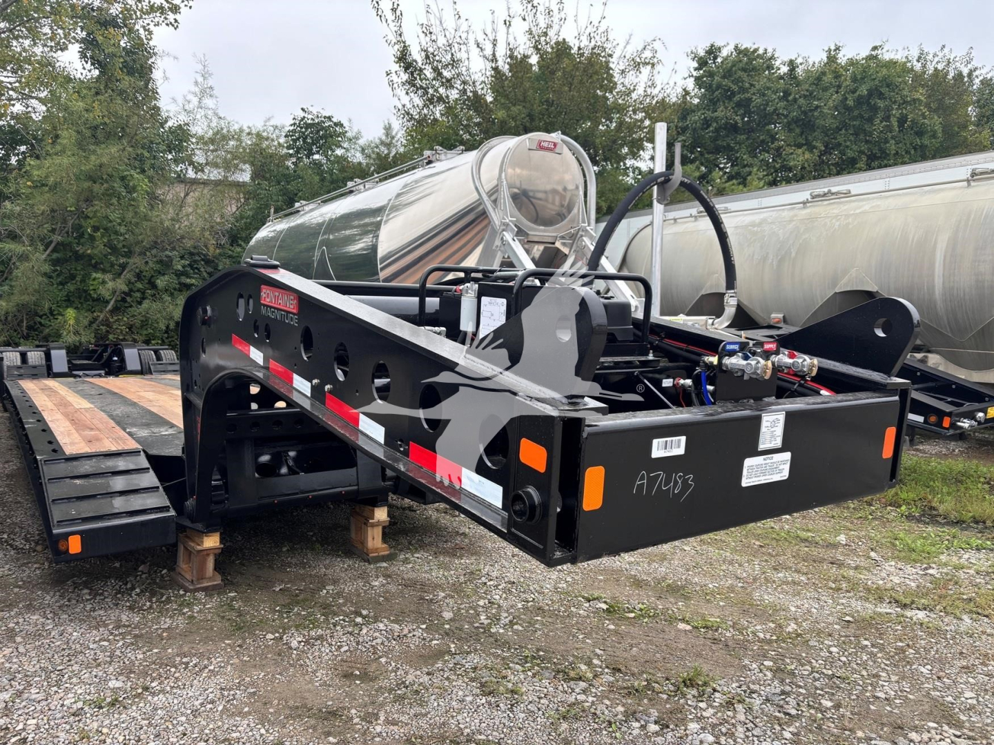 Fontaine lowboy trailer frame showing A75?3 markings, hydraulic lines, and toolkit on black steel with reflective tape; side rails and hitch area visible.