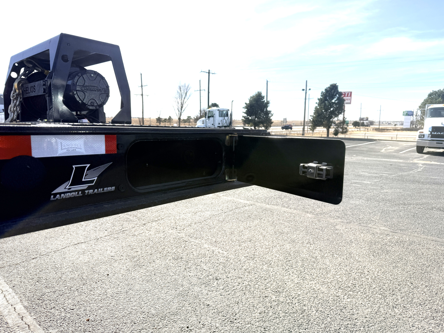 Rear end of a Landoll 440B-53 40 Ton slide axle trailer showing a storage cavity, metal deck, and a small hinge/ latch with a tote or winch mechanism visible.