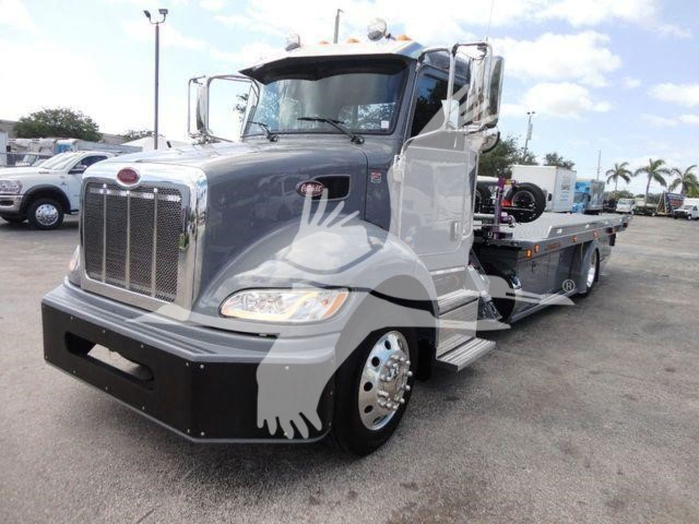 Peterbilt 337 rollback truck in a dealership lot with gray cab and flatbed tow body.