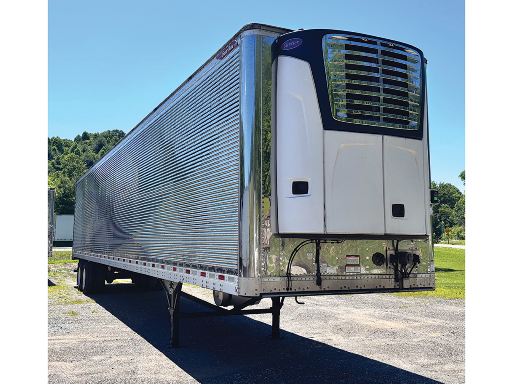 Reefer trailer in-side view with Everest CL refrigeration unit and chrome front legs. Side cargo door corrugated metal design, blue sky, trailer on wheels.