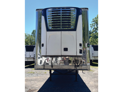Reefer trailer front view showing curved chrome grille, blue top cap, and metal rear with support legs visible.