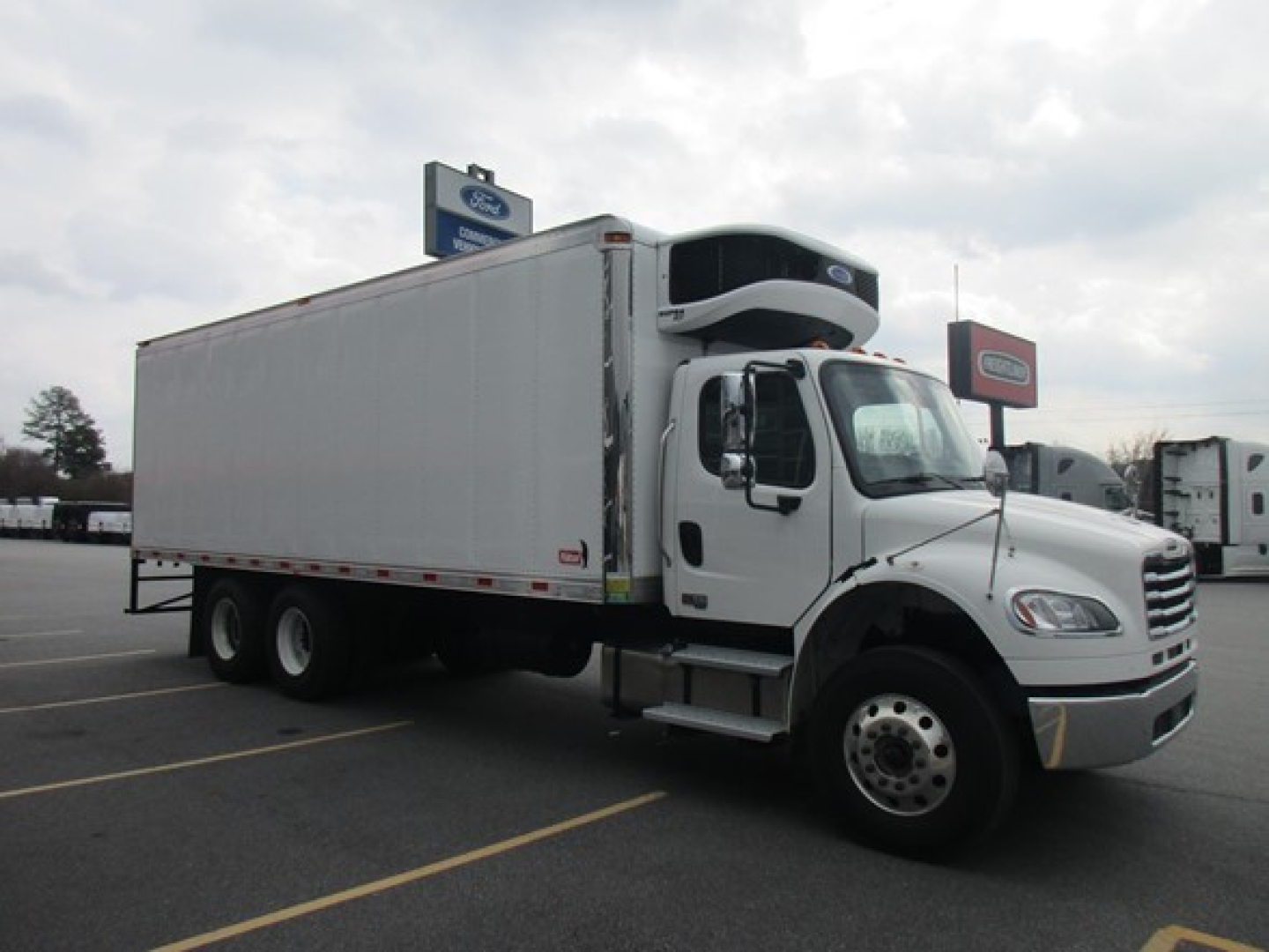 Freightliner Business Class M2 106 Plus refrigerated box truck side view with cab, white exterior, dual rear axles, cargo area, and refrigeration unit on top front of box.