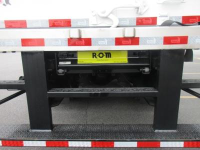 Rear view of a Freightliner M2 106 Plus chassis showing a yellow ROM label on the underbody with reflective red/white striping and black support frame.