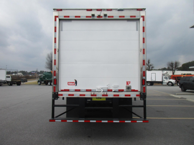 Rear view of a Freightliner M2 106 refrigerated box truck with white cargo doors, red-and-white reflective stripes along edges, and a black bumper. KT2 logos near lower doors.