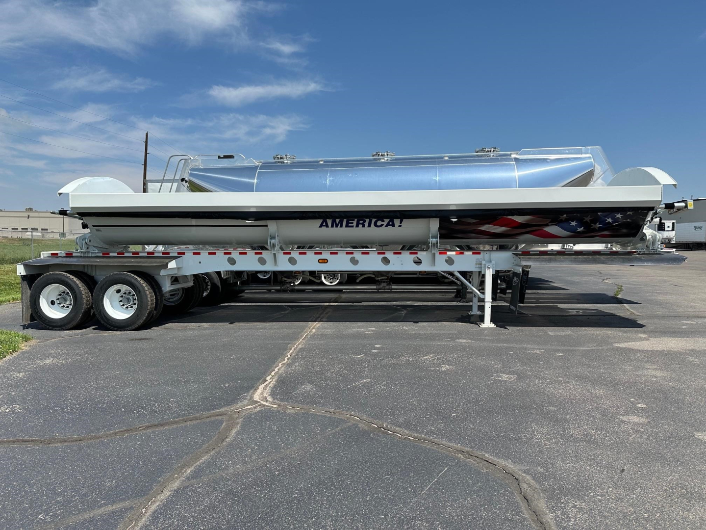 Semi-trailer side dump with aluminum tank and support legs, trailer tires visible, American flag graphic and AMERICA! branding on side