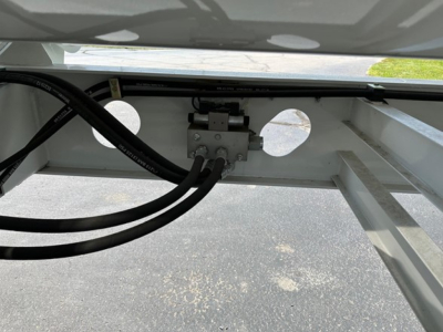 Trailer side dump mounting area showing hydraulic lines and control valve assembly with tubing connected, metal frame and circular cutouts.