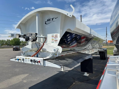 Jet side dump trailer showing hydraulic system and underbody components with US flag design on hopper side panel.
