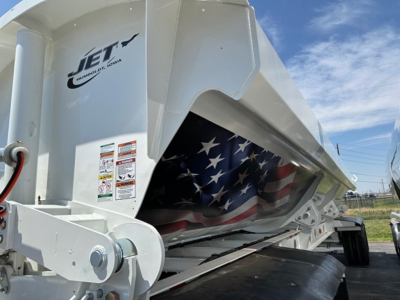 Jet side dump trailer showing white body with folded tarp area and American flag graphic inside the hopper; Jet logo and warning stickers visible on the front panel.