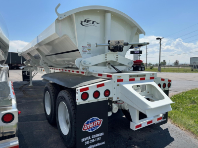 Dump trailer rear and side view showing Jet brand side-dump bed with white paint, dual rear axles, reflective tape, and ladder/access platform.