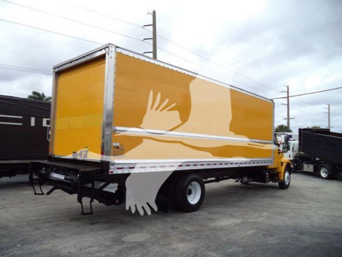 Box truck cargo area of a 2019 International Durastar 4300 in yellow with art on side showing white shapes; rear view with truck cab visible.