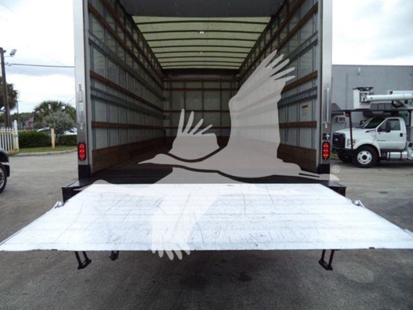 Back view of a 2019 International Durastar 4300 box truck with a lowered aluminum ramp at the rear, interior cargo space visible, stock trailer yard.
