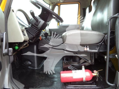 Interior of a 2019 International Durastar 4300 cab showing steering wheel, driver's seat, dashboard, pedals, and a red fire extinguisher mounted under the seat area.