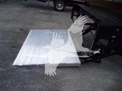 Platform with aluminum ramp or plate on ground near a truck chassis; visible text not legible due to watermark; overall shows a metal plate and part of a vehicle frame.