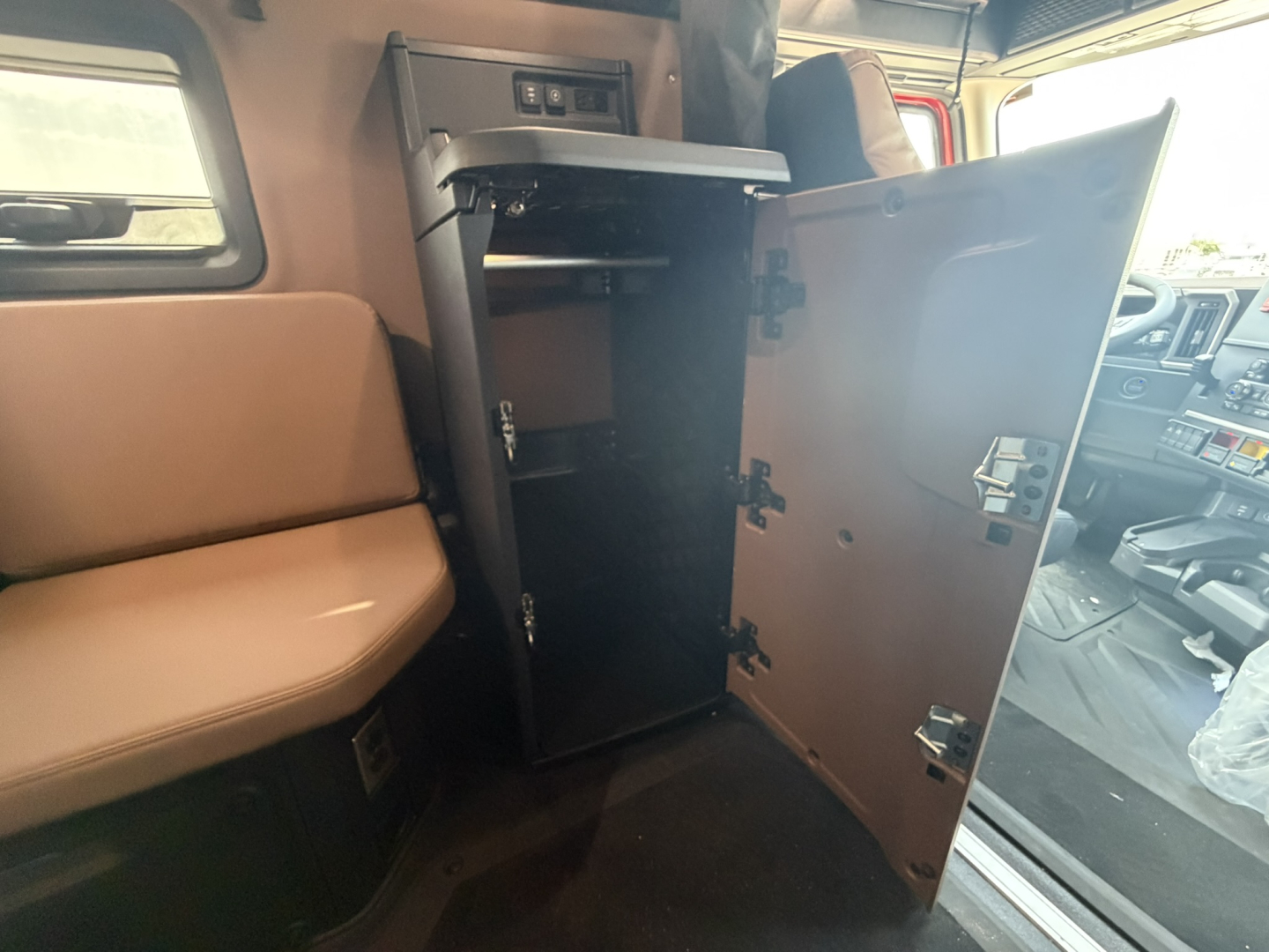 Cabin interior of a 2027 Mack PR64T76H with a tall cabinet/open cabinet door revealing empty storage space, part of the sleeper truck interior.