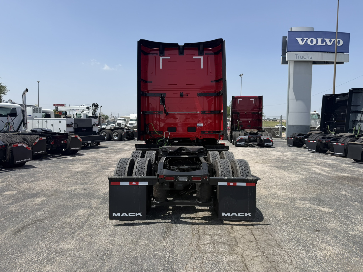 Mack PR64T76H tractor with red cab raised, rear view showing fifth wheel and dual rear axles in a truck lot.
