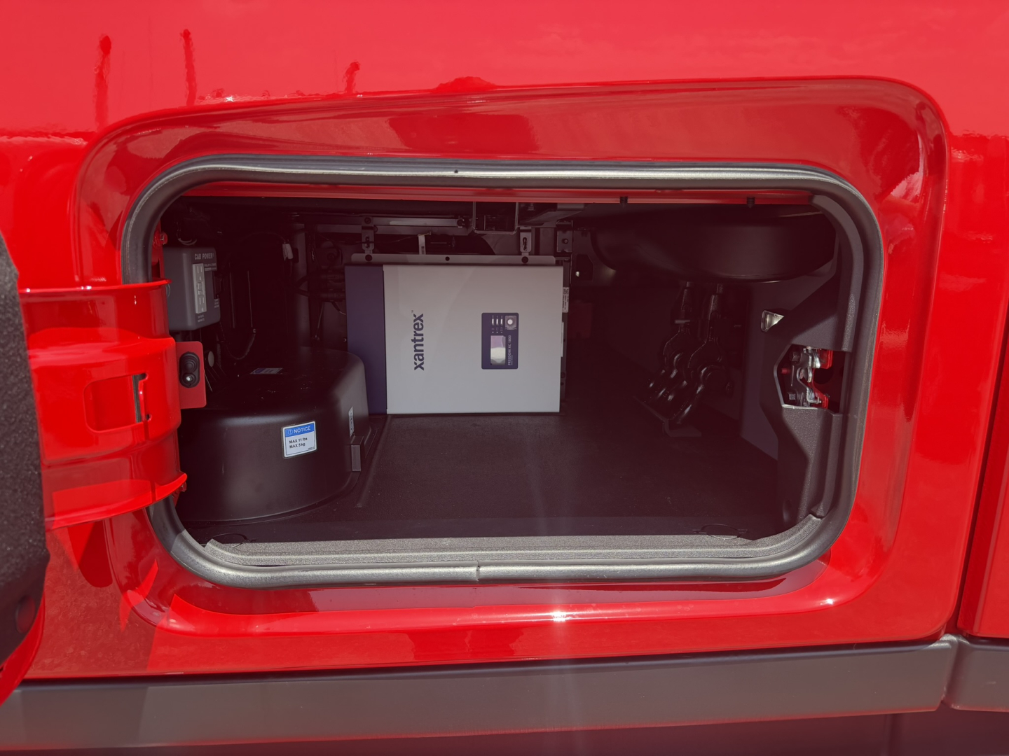 Truck cab area showing storage compartment with a white Xantrex box and other equipment inside the bay.