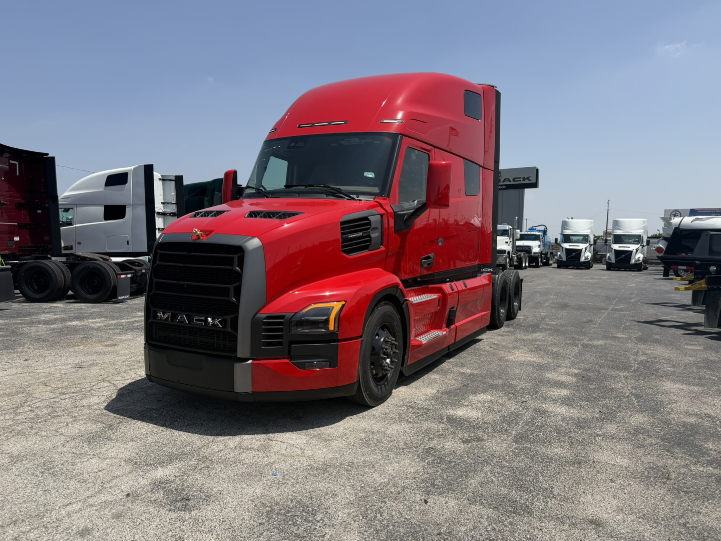 Red Mack tractor-trailer in a dealership lot, front-left view. Visible text includes 'MACK' on grille and no other legible labels.