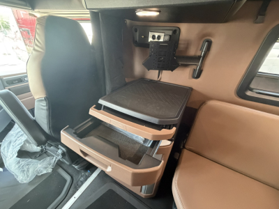 Truck cab interior with a fold-out sleeper area and storage compartments; beige and brown tones; mounted monitor/display bracket on back wall; seat and side panel visible.