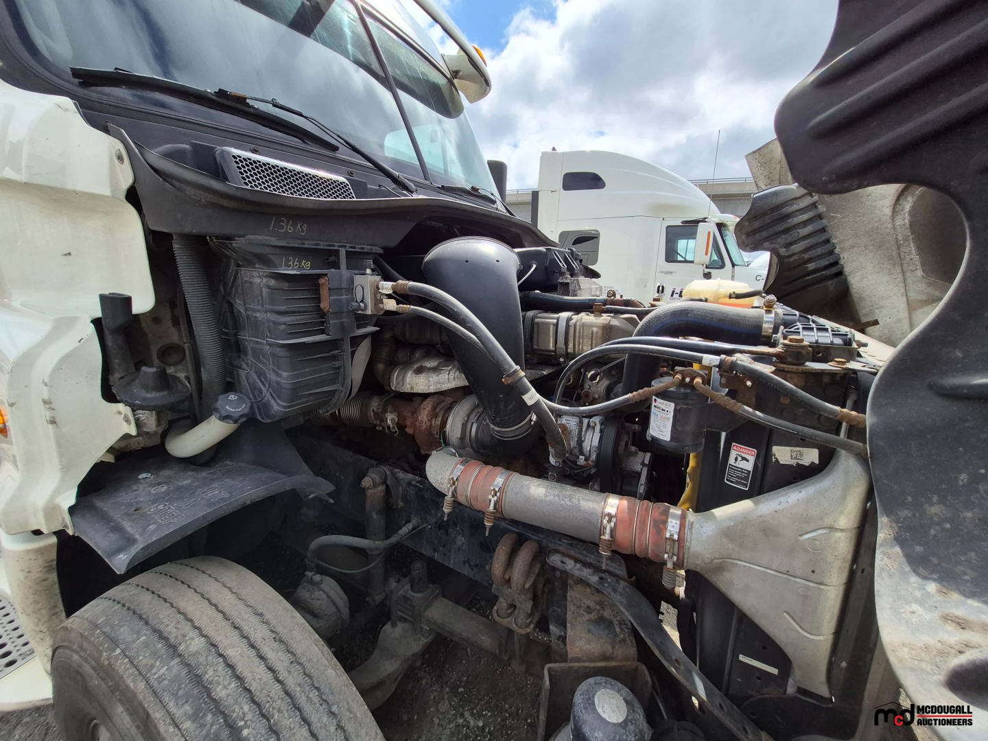 Freightliner Cascadia engine bay showing turbo intake, hoses, coolant reservoir, and battery with visible wiring.