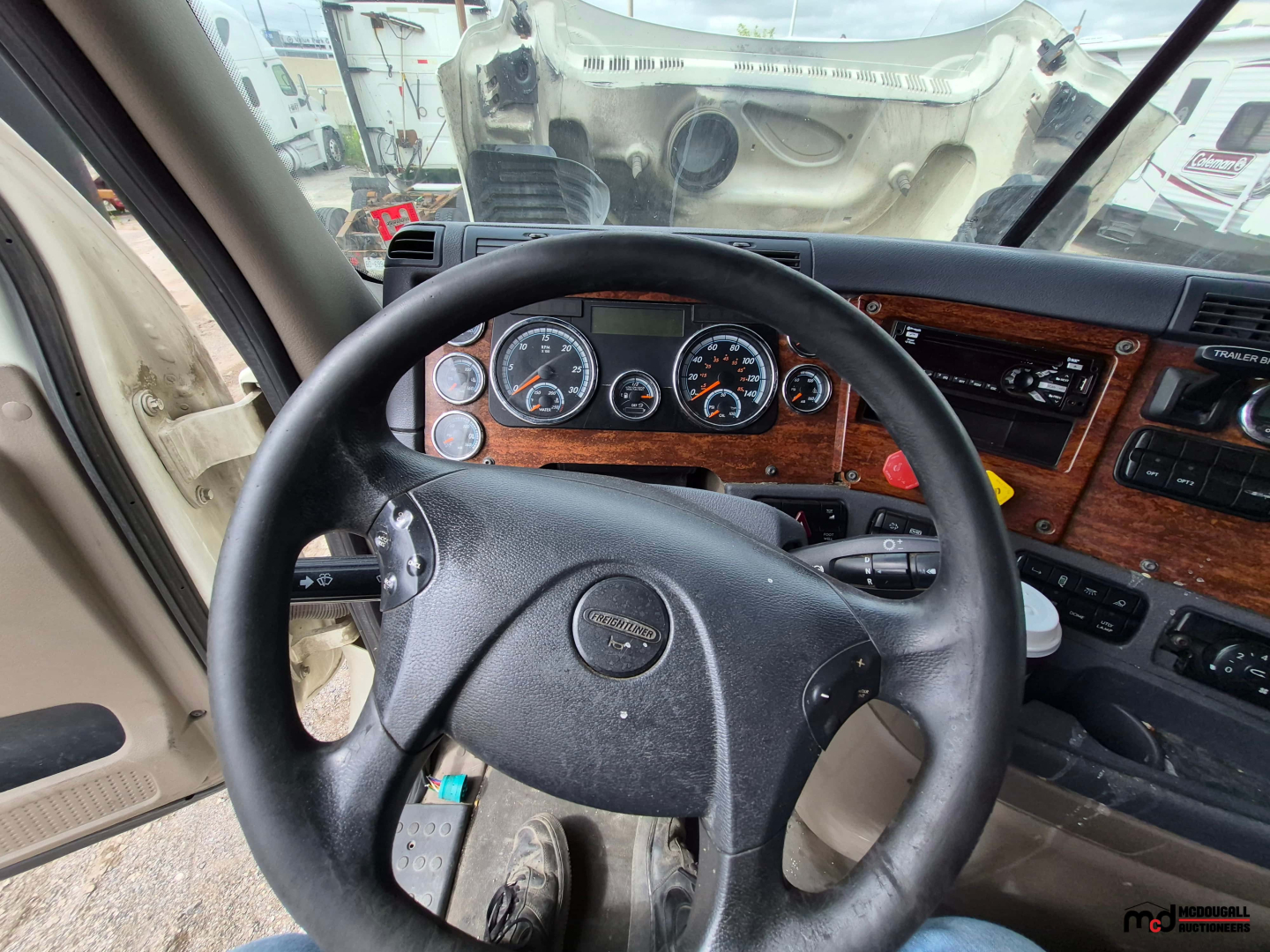 Freightliner Cascadia truck interior view showing steering wheel and dashboard with analog gauges and wood-grain panels.