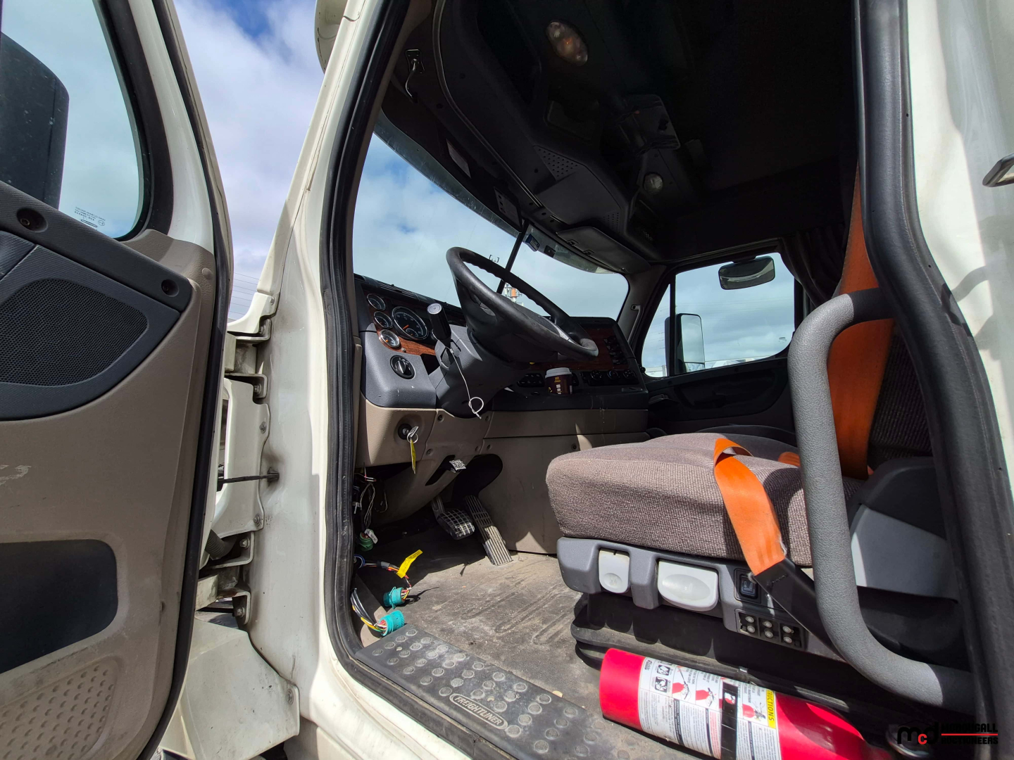 Truck cab interior of a 2017 Freightliner Cascadia T/A with open driver door showing steering wheel, dashboard, and orange seat belt.