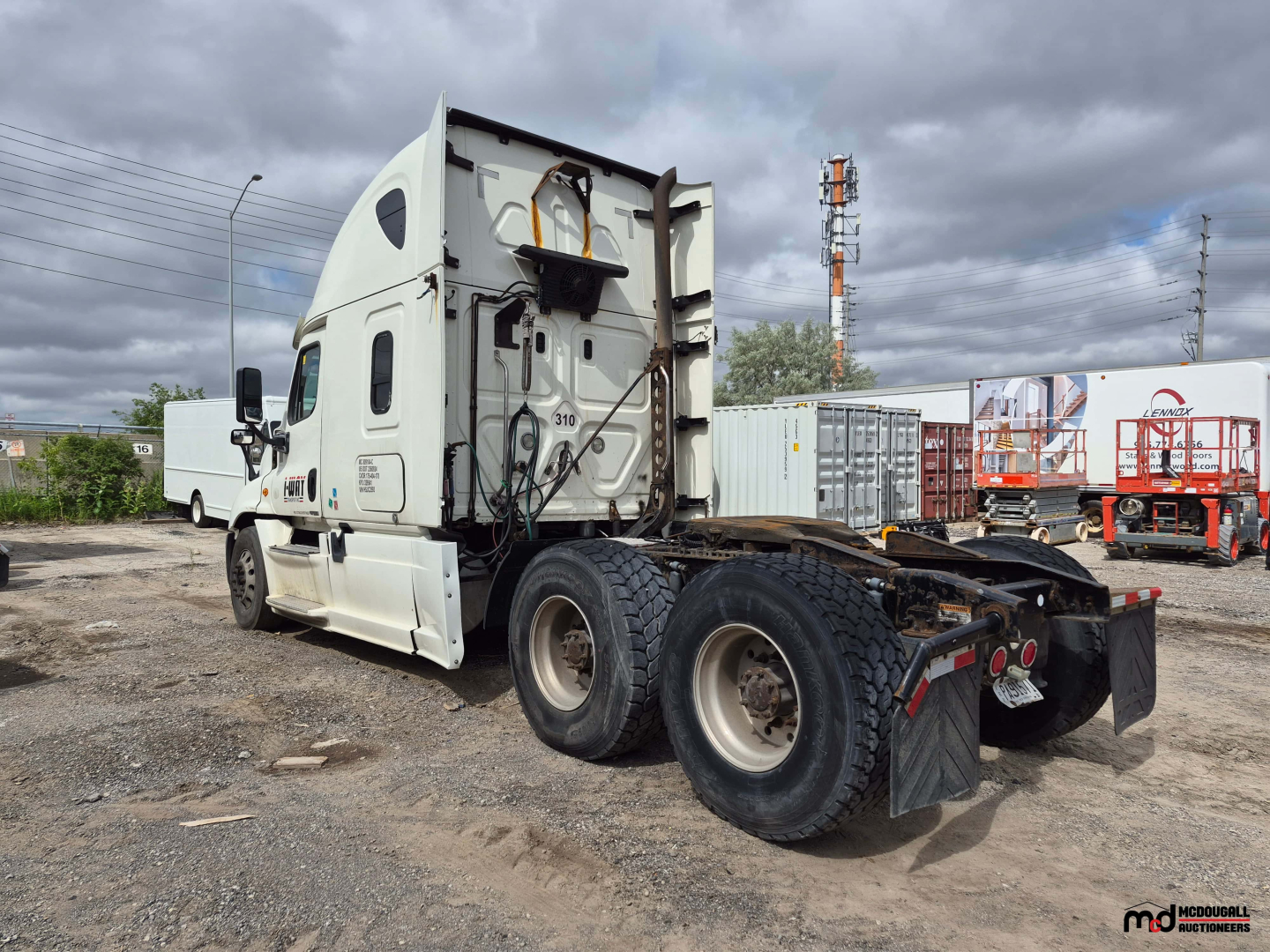 Freightliner Cascadia tractor rear/side view showing chassis and cab with fifth wheel mount removed; notations on cab and mudflaps, multiple tires, and parking lot background.