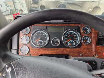 Freightliner Cascadia dashboard with wood grain panel, showing multiple gauges and steering wheel in view.