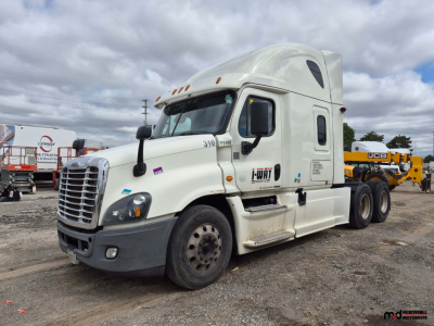 Freightliner Cascadia tandem tractor cab in view showing front grille, headlights, and side mirrors; white exterior with sleeper cab and rear coupling visible.