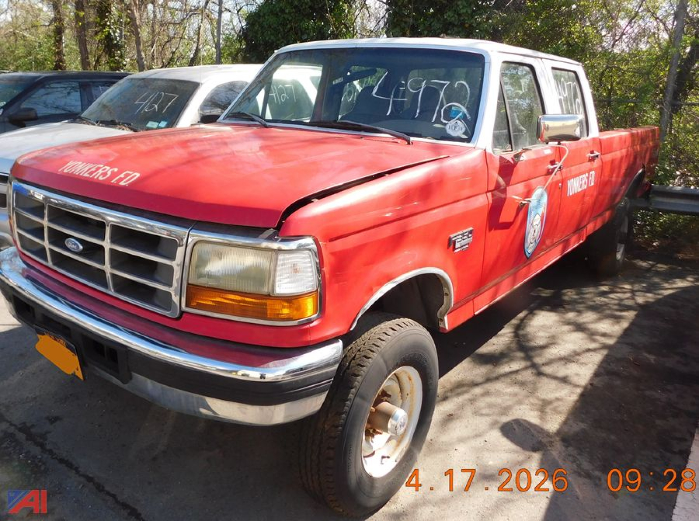 Ford F-350 pickup truck side view front-left showing red body, white cab, chrome bumper, and writing on windshield and doors.