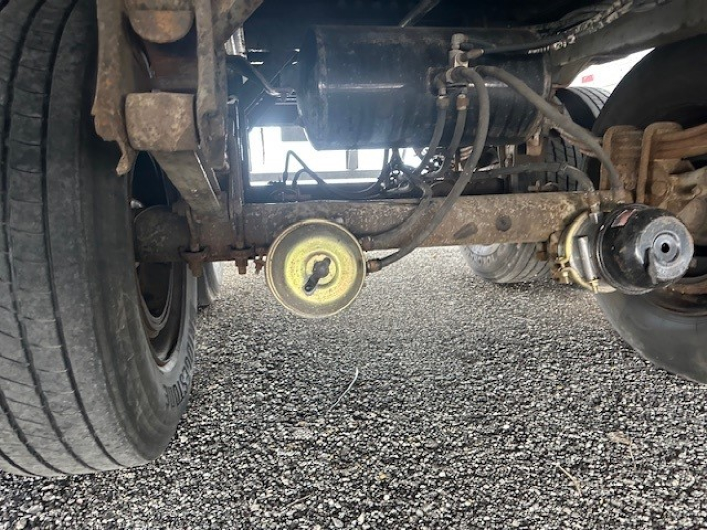Underneath view of a 2014 Wabash trailer hitch area showing axle, suspension, air line, and circular yellow access cap.