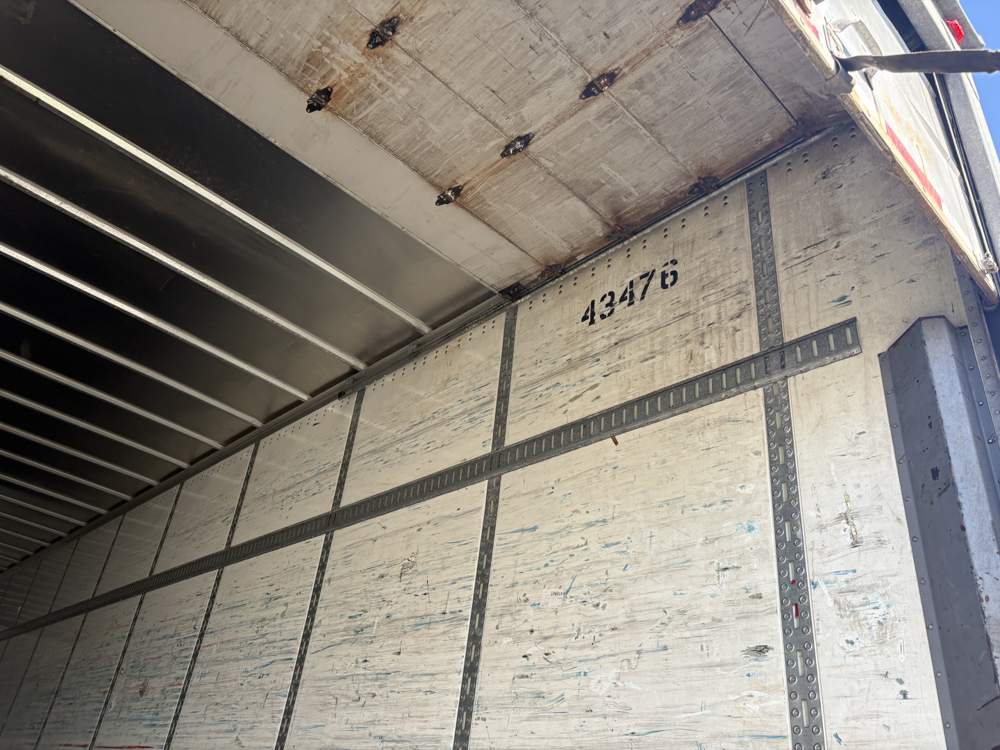 Trailer interior wall with vertical and horizontal metal tracks, stamped number 432176, worn plywood surface, van trailer cargo area.