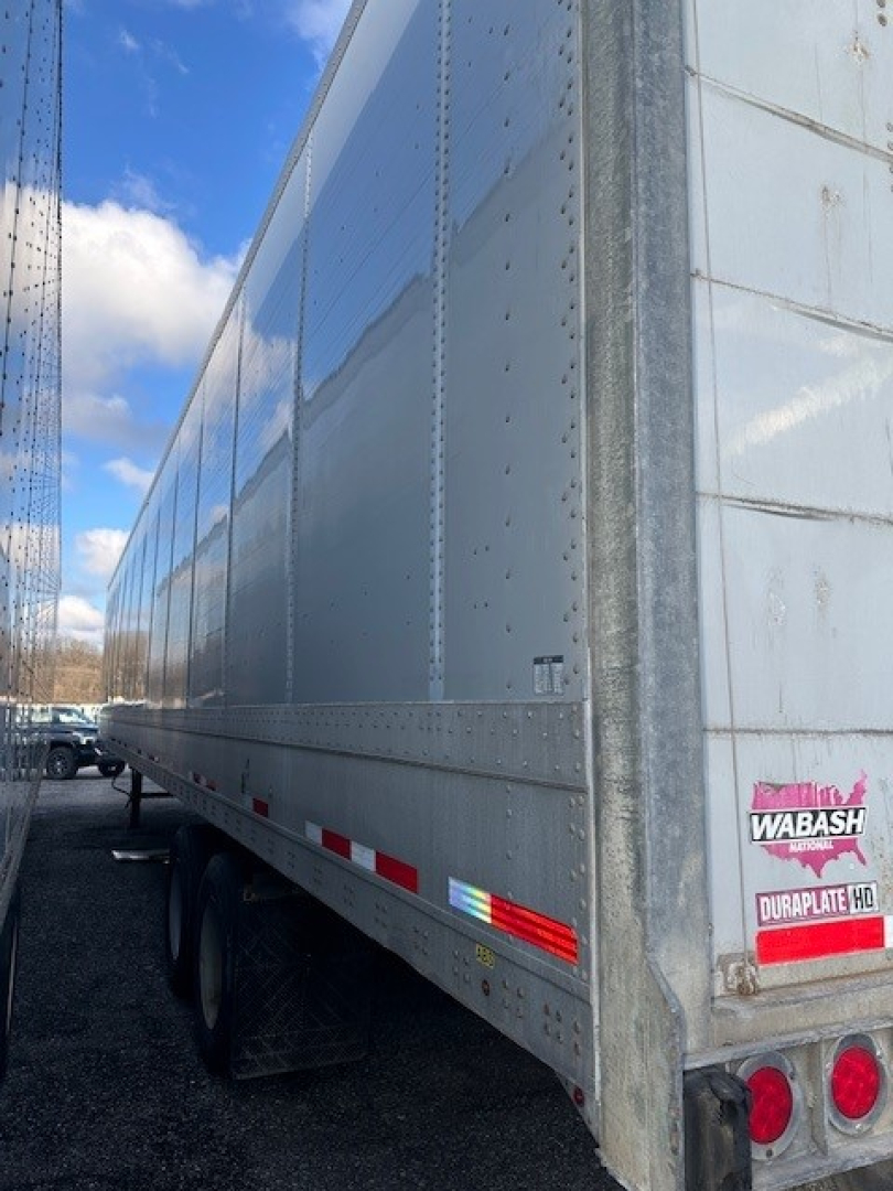 Trailer side view showing aluminum roll-door trailer with riveted panels and Wabash logo sticker on rear corner.