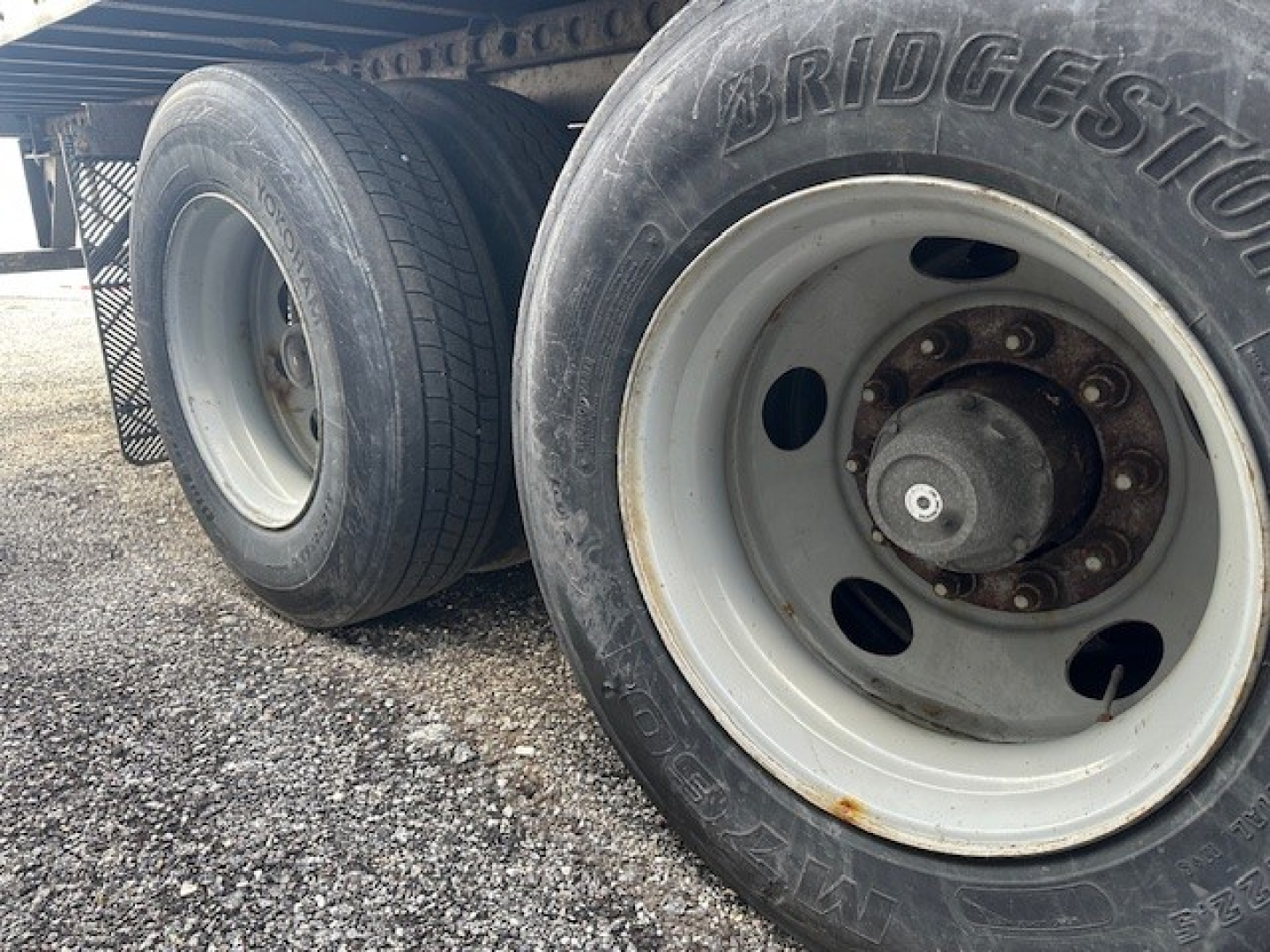 Truck trailer wheel assembly showing Bridgestone tire and white steel rim with lug nuts, side view of tandem axle.