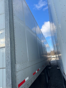 Trailer side view showing a 2014 Wabash roll door trailer with riveted metal panels and reflective red/white side markings.