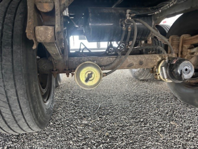 Underneath view of a 2014 Wabash trailer hitch area showing axle, suspension, air line, and circular yellow access cap.